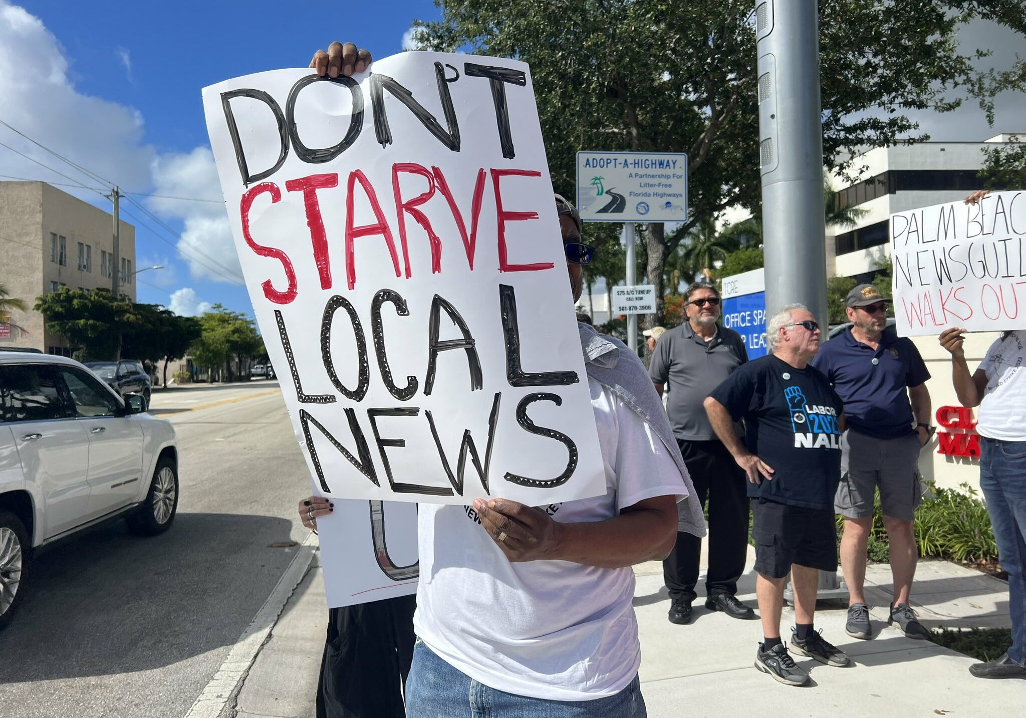 Photo of person holding sign at a rally during a strike at Gannett that reads, "Don't starve local news." Other workers and supporters are in the background with one sign that reads "Palm Beach NewsGuild walks out"