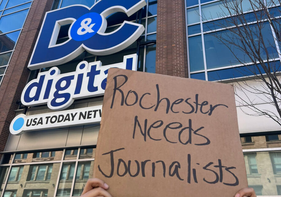A striker holds up a sign "Rochester needs journalists" in front of the Rochester Democrat and Chronicle building in New York.