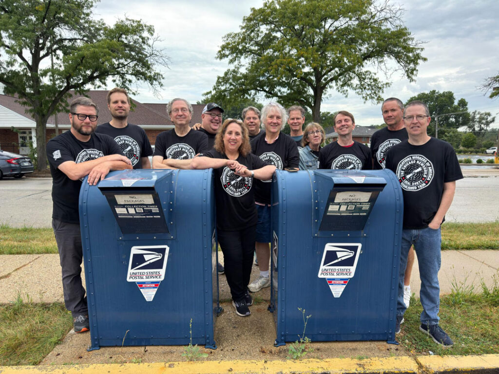 Workers at the Daily Herald pose in front of USPS mailboxes